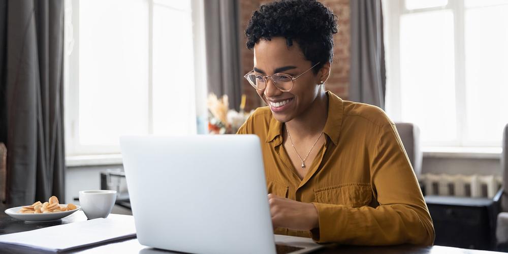 A young woman wearing glasses smiles while looking at her laptop.