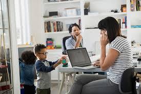 A mother is working from home while her two young children play nearby.